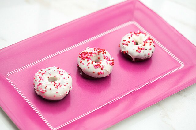 These little donuts contain extra cocoa powder for a more chocolatey red velvet. A cream cheese glaze and lots of sprinkles make them extra cute! | www.spachethespatula.com #recipe