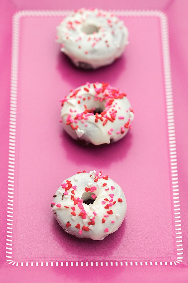 These little donuts contain extra cocoa powder for a more chocolatey red velvet. A cream cheese glaze and lots of sprinkles make them extra cute! | www.spachethespatula.com #recipe