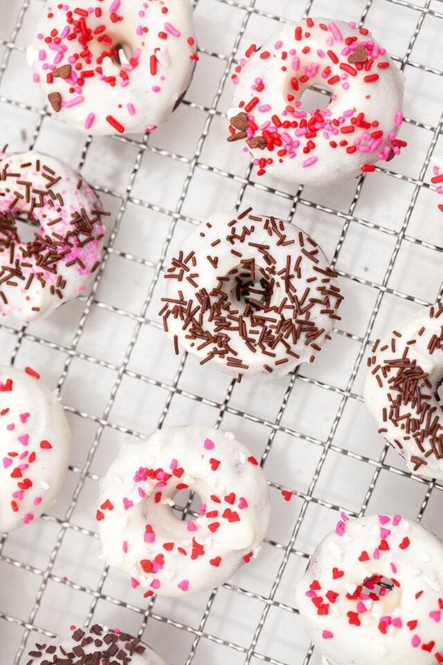 These little donuts contain extra cocoa powder for a more chocolatey red velvet. A cream cheese glaze and lots of sprinkles make them extra cute! | www.spachethespatula.com #recipe