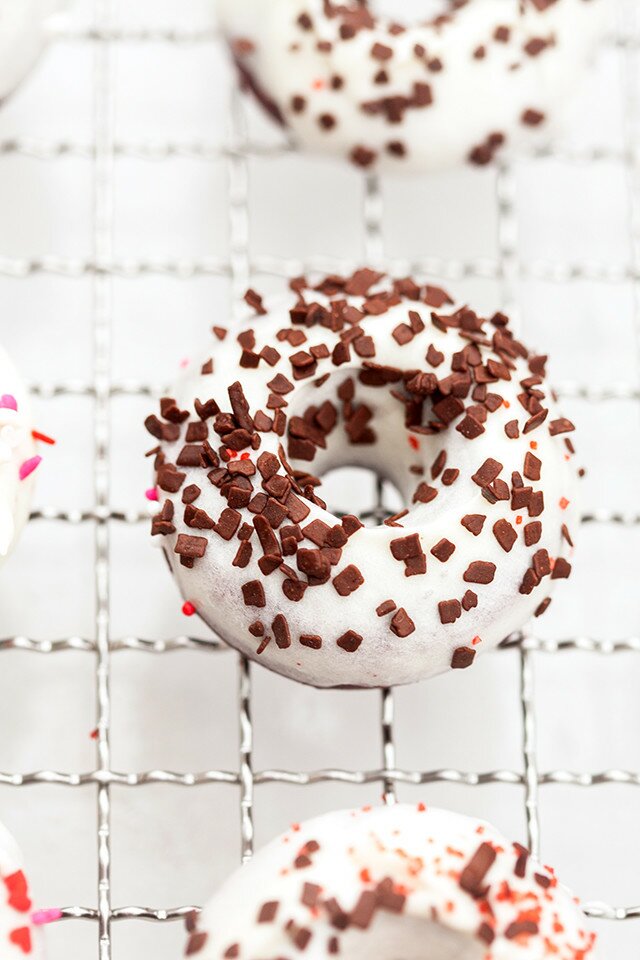 These little donuts contain extra cocoa powder for a more chocolatey red velvet. A cream cheese glaze and lots of sprinkles make them extra cute! | www.spachethespatula.com #recipe