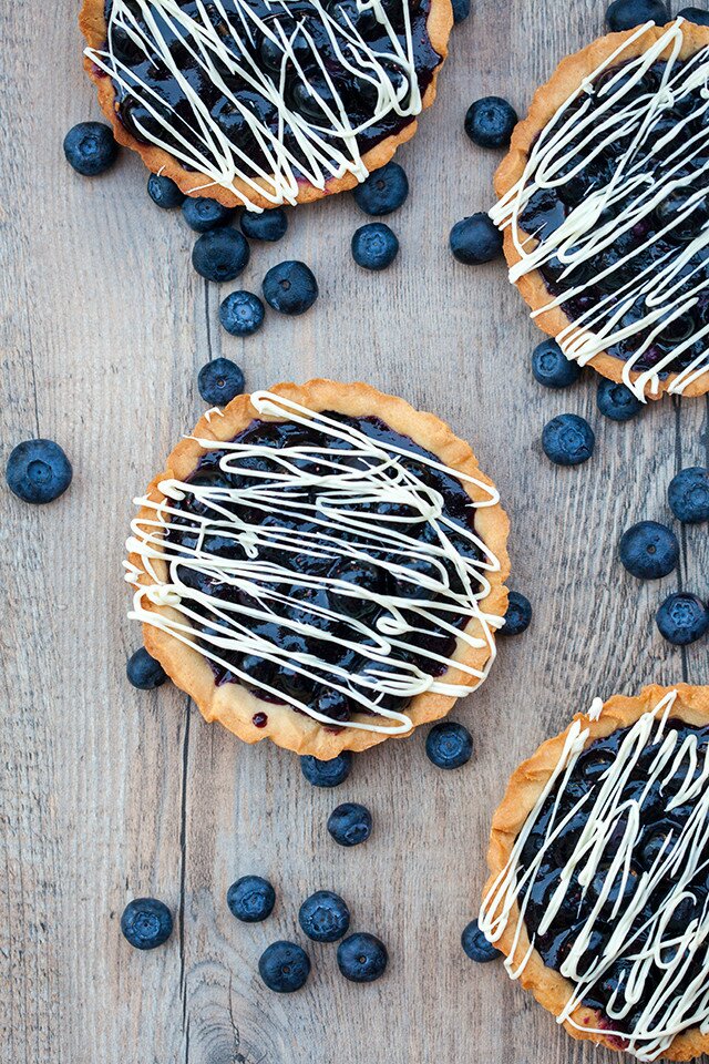 Buttery, crunchy tart shells filled with gooey, fresh blueberry filling and a white chocolate drizzle! | spachethespatula.com #recipe