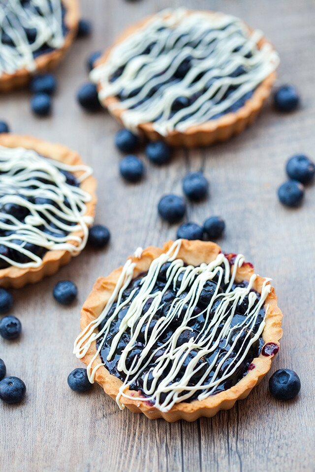 Buttery, crunchy tart shells filled with gooey, fresh blueberry filling and a white chocolate drizzle! | spachethespatula.com #recipe